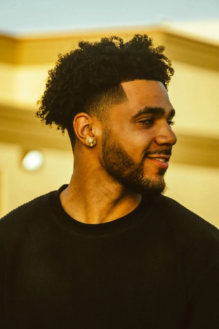 Taper fade discret autour des tempes, cheveux bouclés et barbe courte