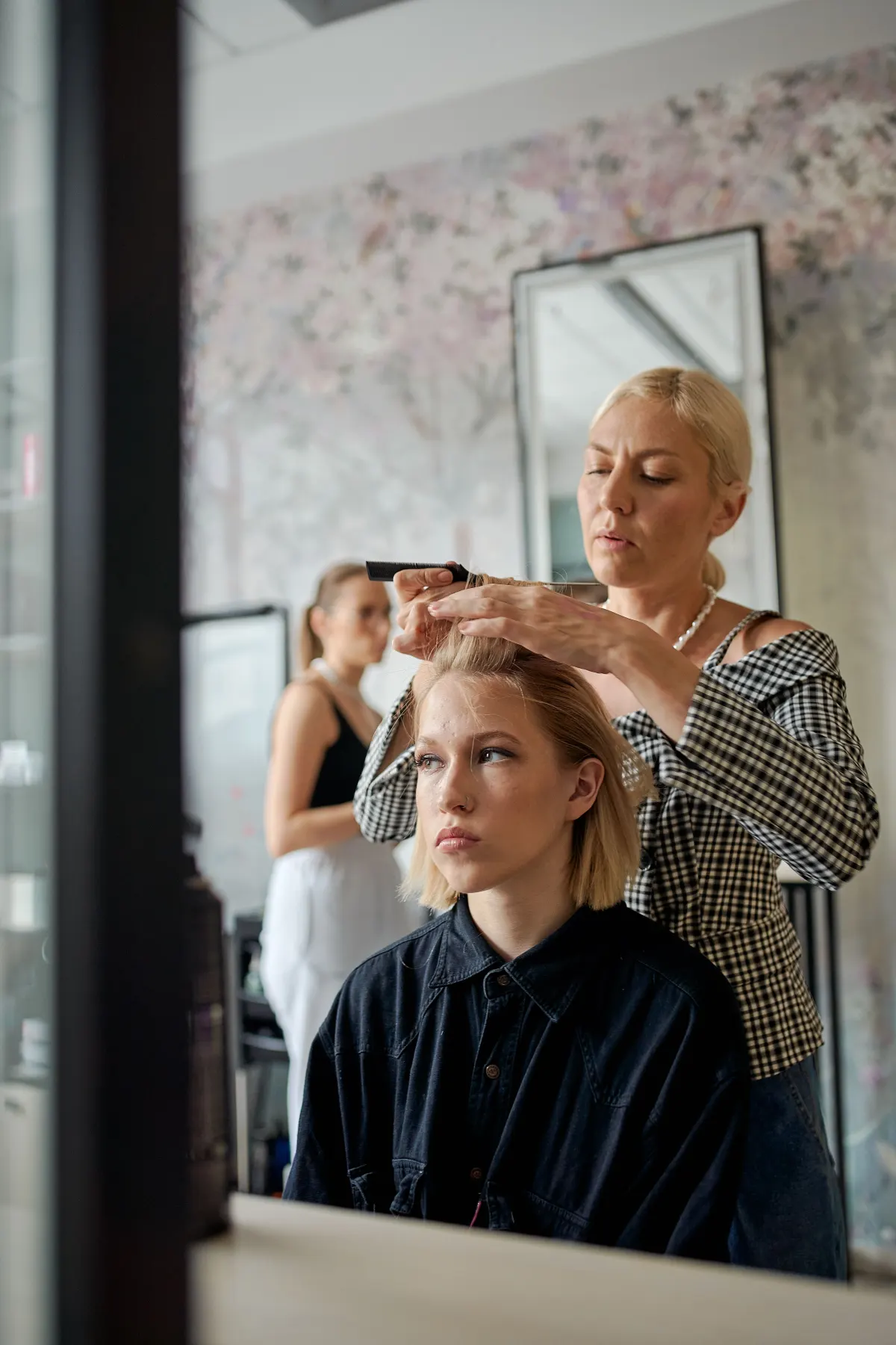 Une coiffeuse ajuste la coupe au carré d’une jeune cliente, face au miroir