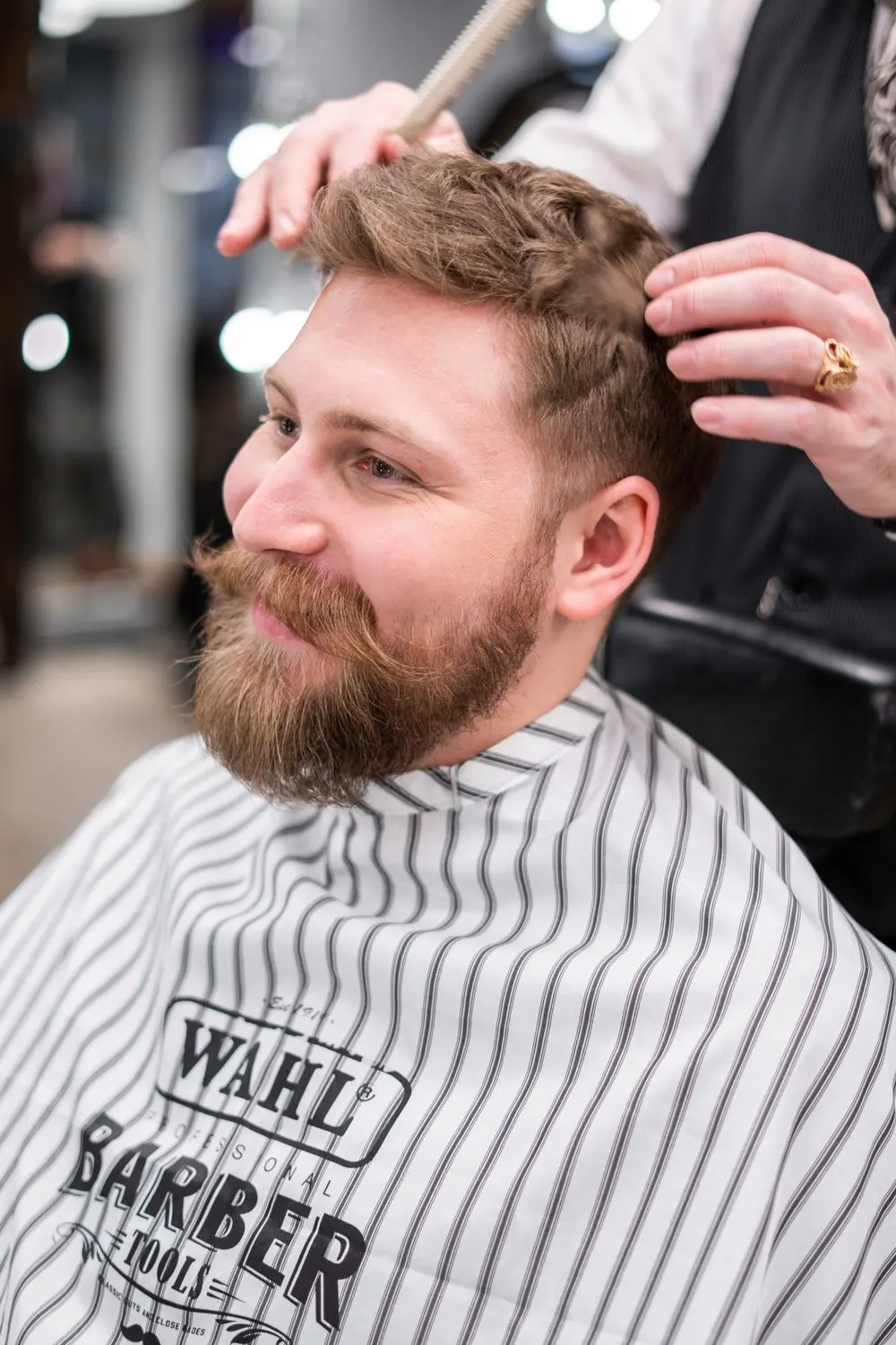 Homme souriant à la barbe taillée, coupe mi-longue coiffée en arrière