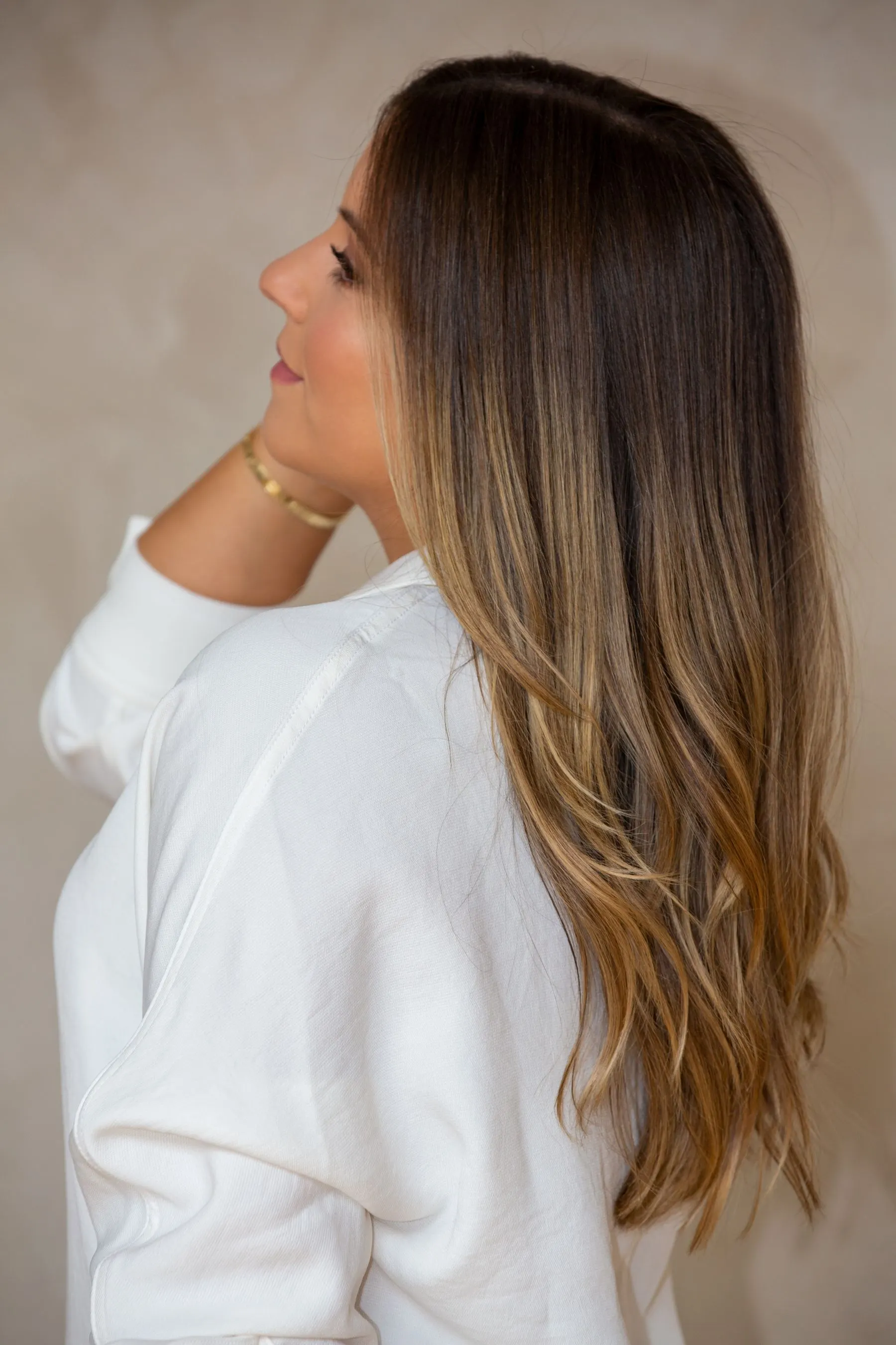 Profil d’une femme aux longs cheveux châtains éclaircis d’un balayage miel, ondulations souples
