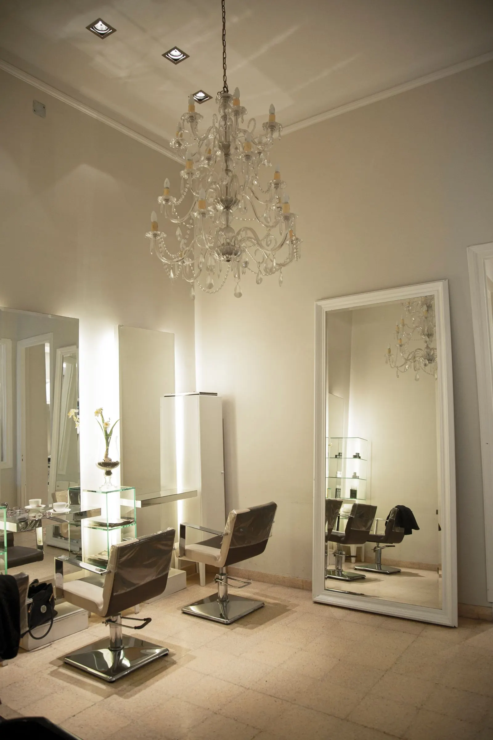 Le salon : grands miroirs, fauteuils clairs et lustre en cristal sous une lumière douce