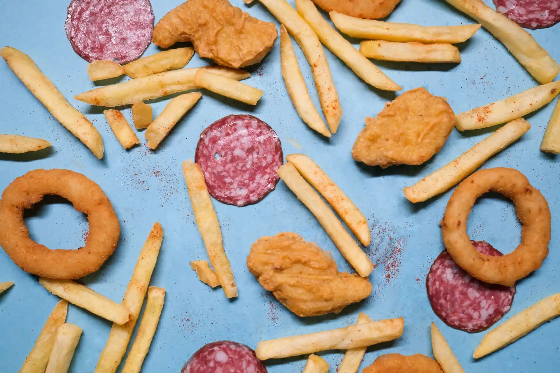 Frites, nuggets et onion rings disposés à plat sur un fond bleu