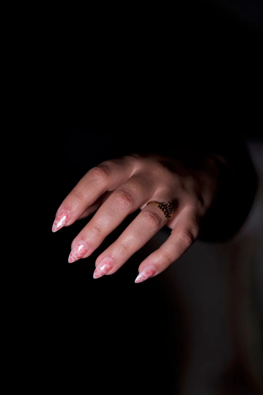 Ongles amande rose poudré sur fond noir, bague fine