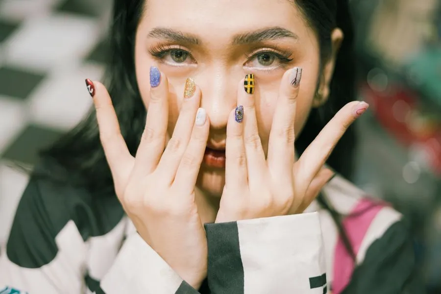 Portrait de Maya, mains devant le visage, nail art graphique coloré