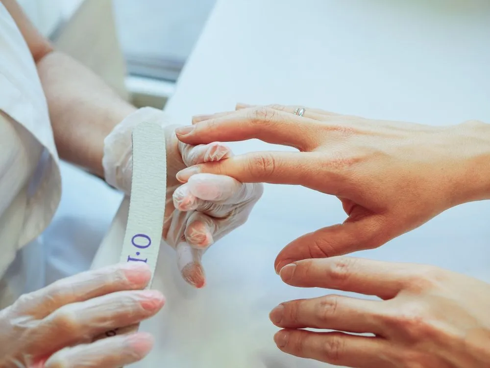 La nail artist, gantée, examine et lime les ongles