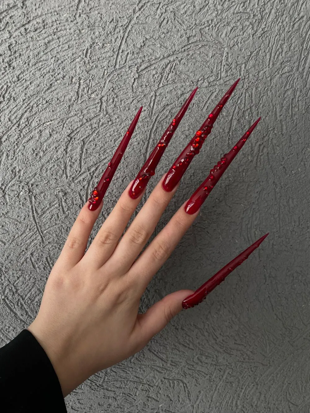Extensions stiletto rouge profond contre un mur texturé