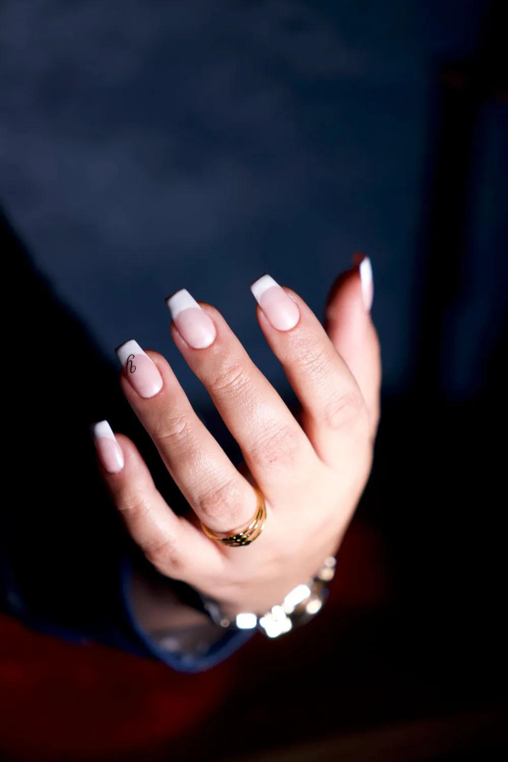 French sur ongles longs, bracelet et bague dorés, fond sombre