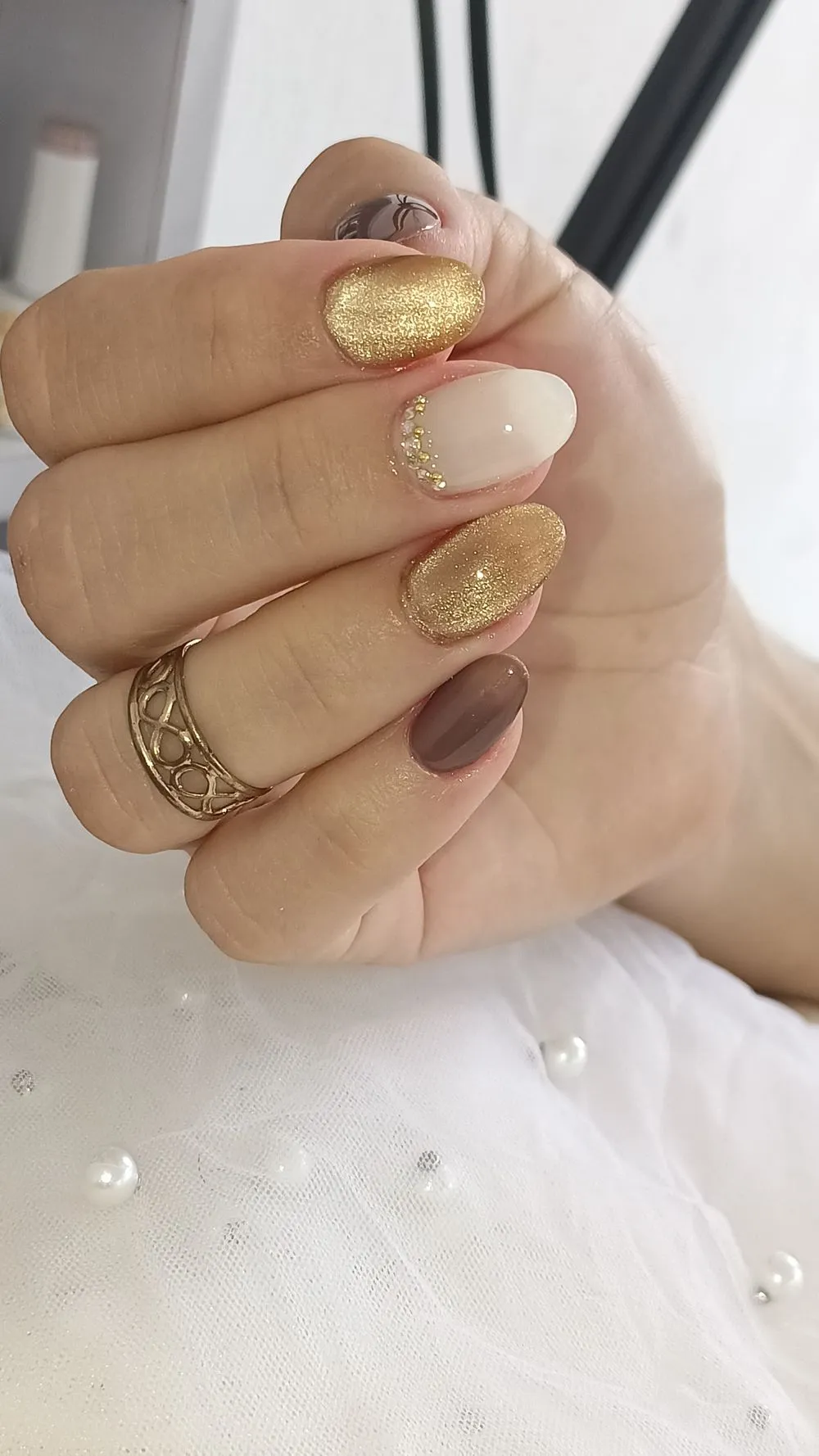 Ongles glazed dorés, nude et chocolat sur une main baguée