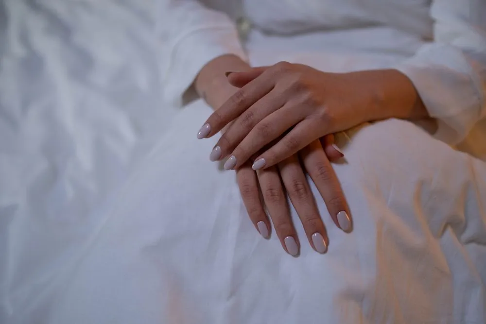 Mains croisées sur une robe blanche, ongles nude brillants
