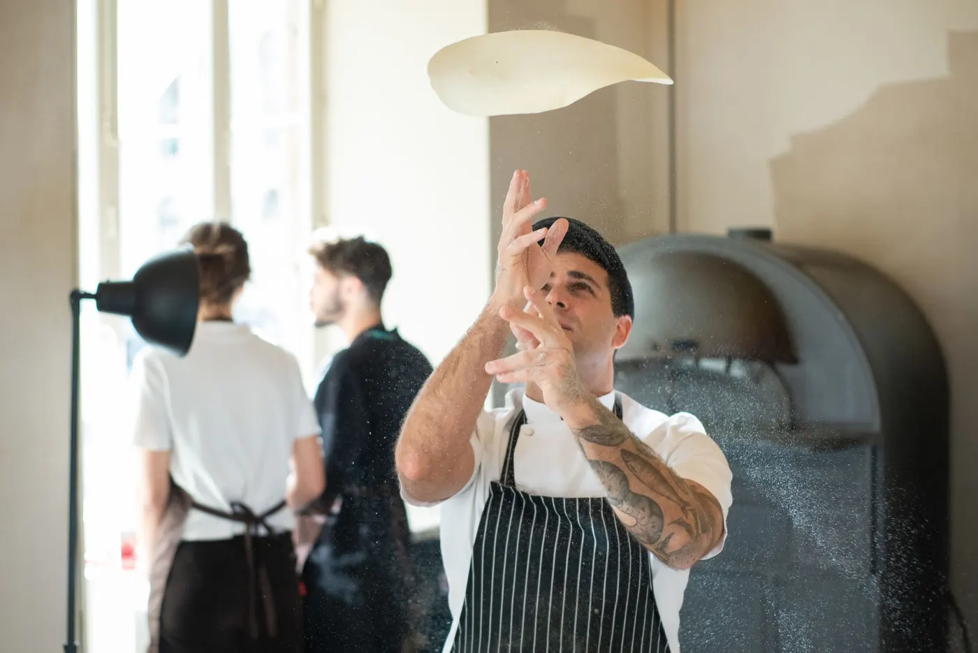 Pizzaiolo qui lance un pâton en l’air dans la cuisine ouverte