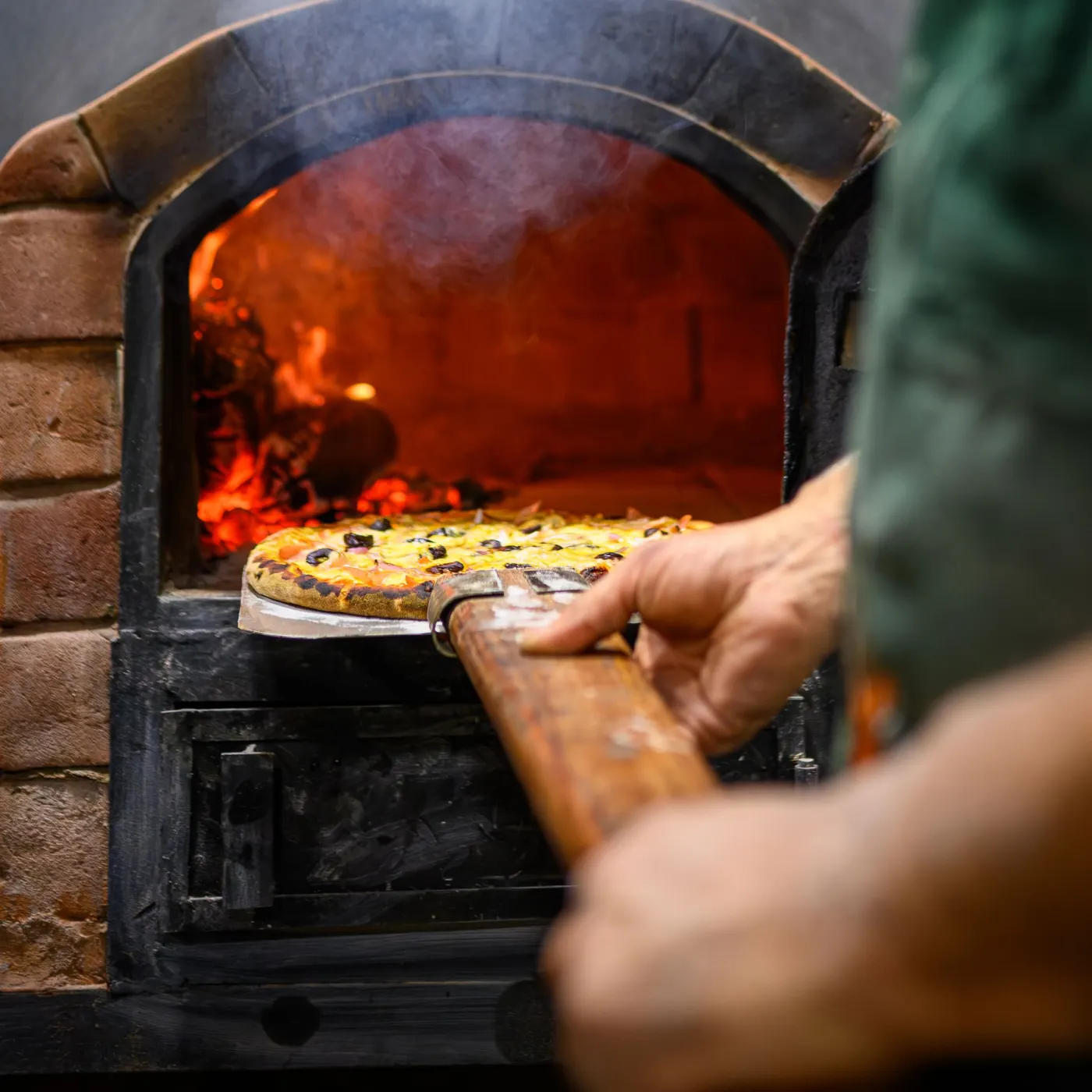 Pizza enfournée à la pelle dans le four à bois