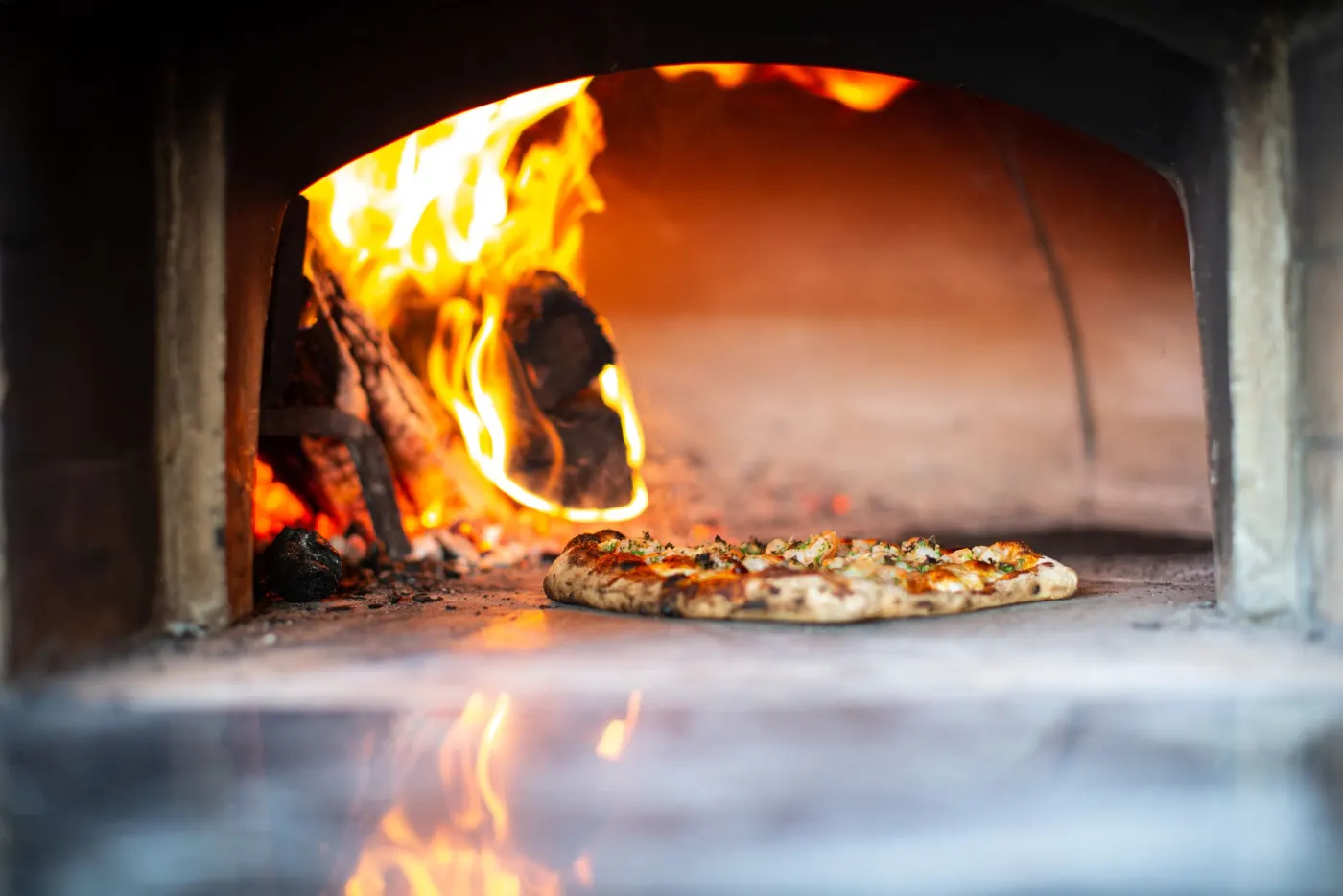 Flammes du four à bois derrière une pizza en cuisson