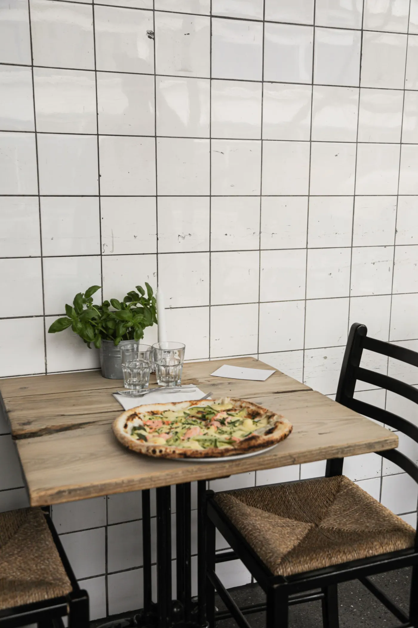 Pizza servie sur une table en bois clair devant un mur carrelé