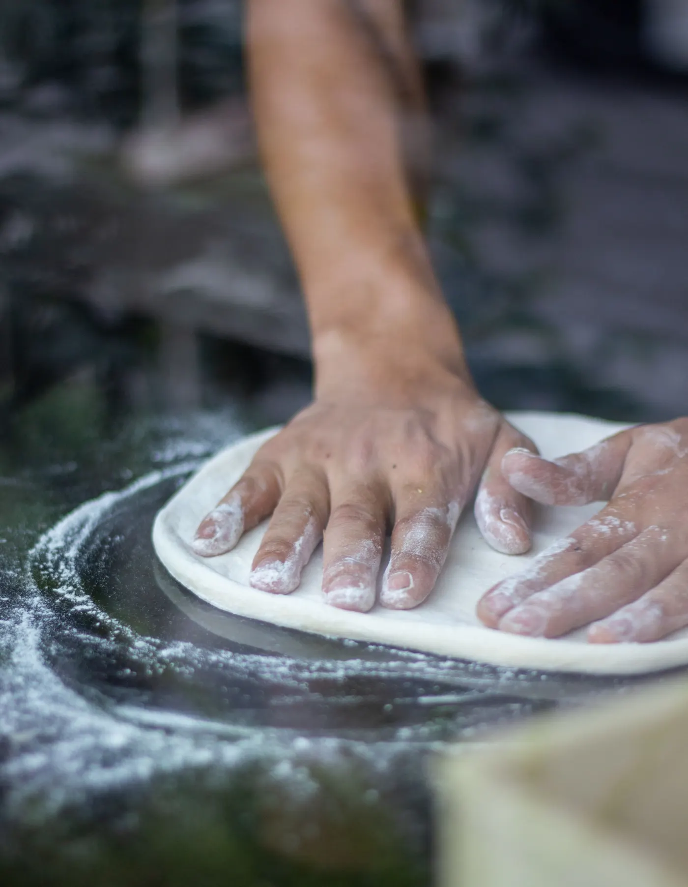 Mains qui travaillent la pâte à pizza sur un plan fariné
