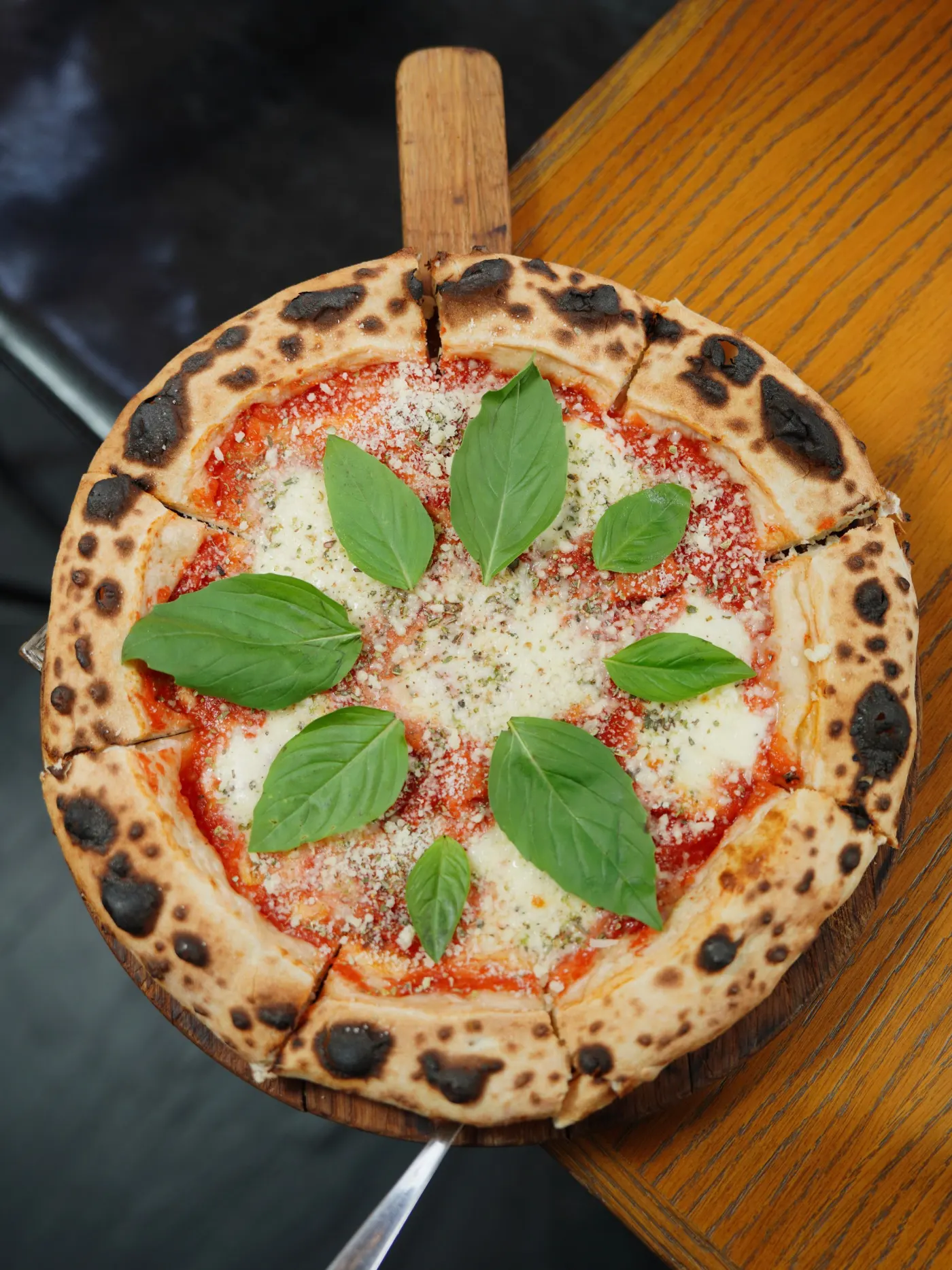 La pizza signature entière sur sa pelle en bois, bord soufflé et taches de cuisson