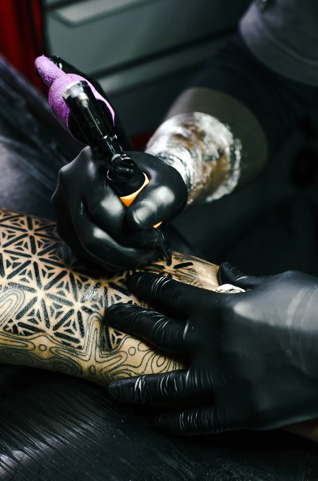 Fleur de vie géométrique en cours de tatouage sur l’avant-bras, gants noirs