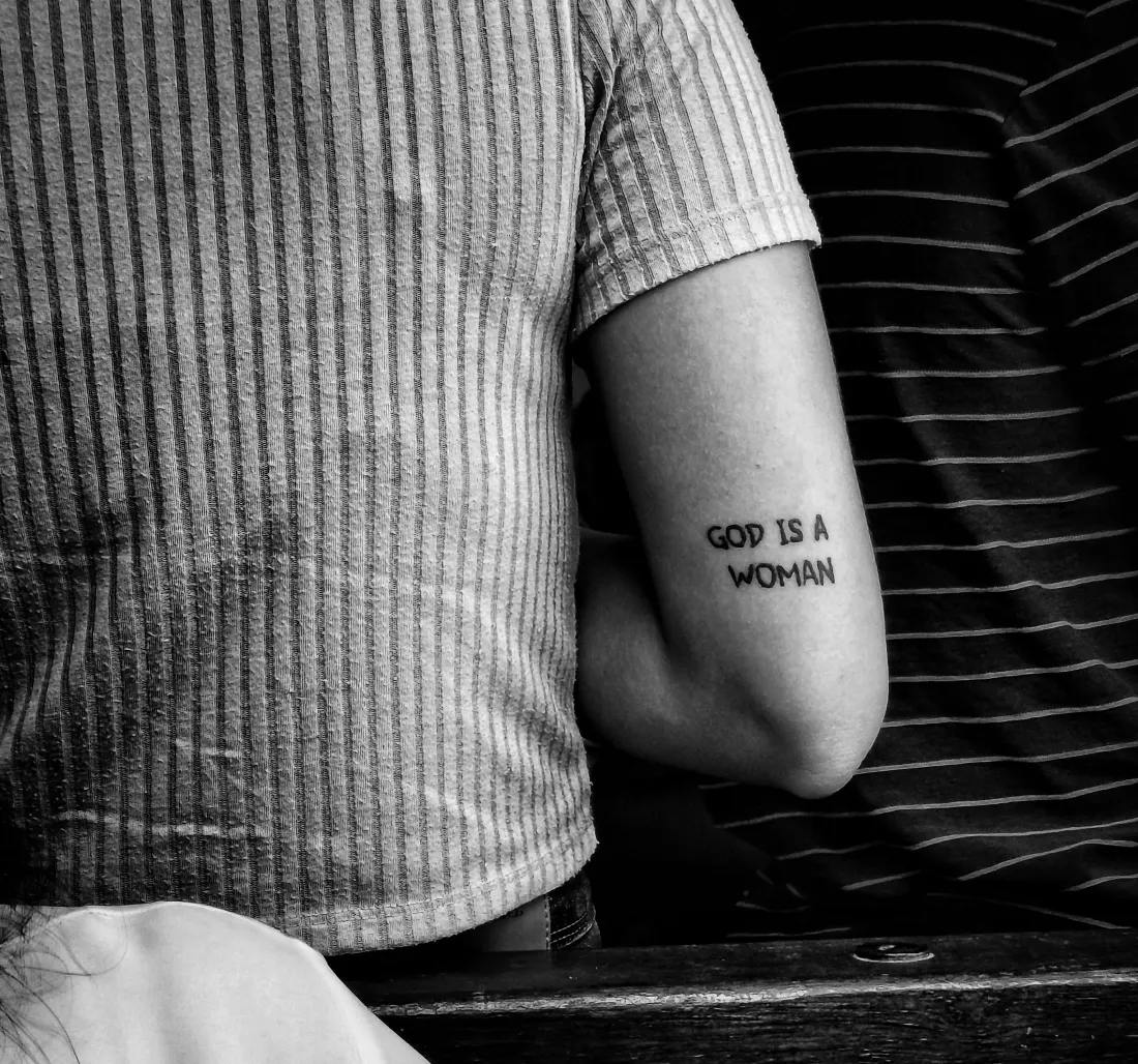 Phrase « God is a woman » en petites capitales à l’arrière du bras