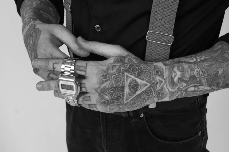 Mains tatouées de motifs ornementaux en noir et blanc, montre en acier
