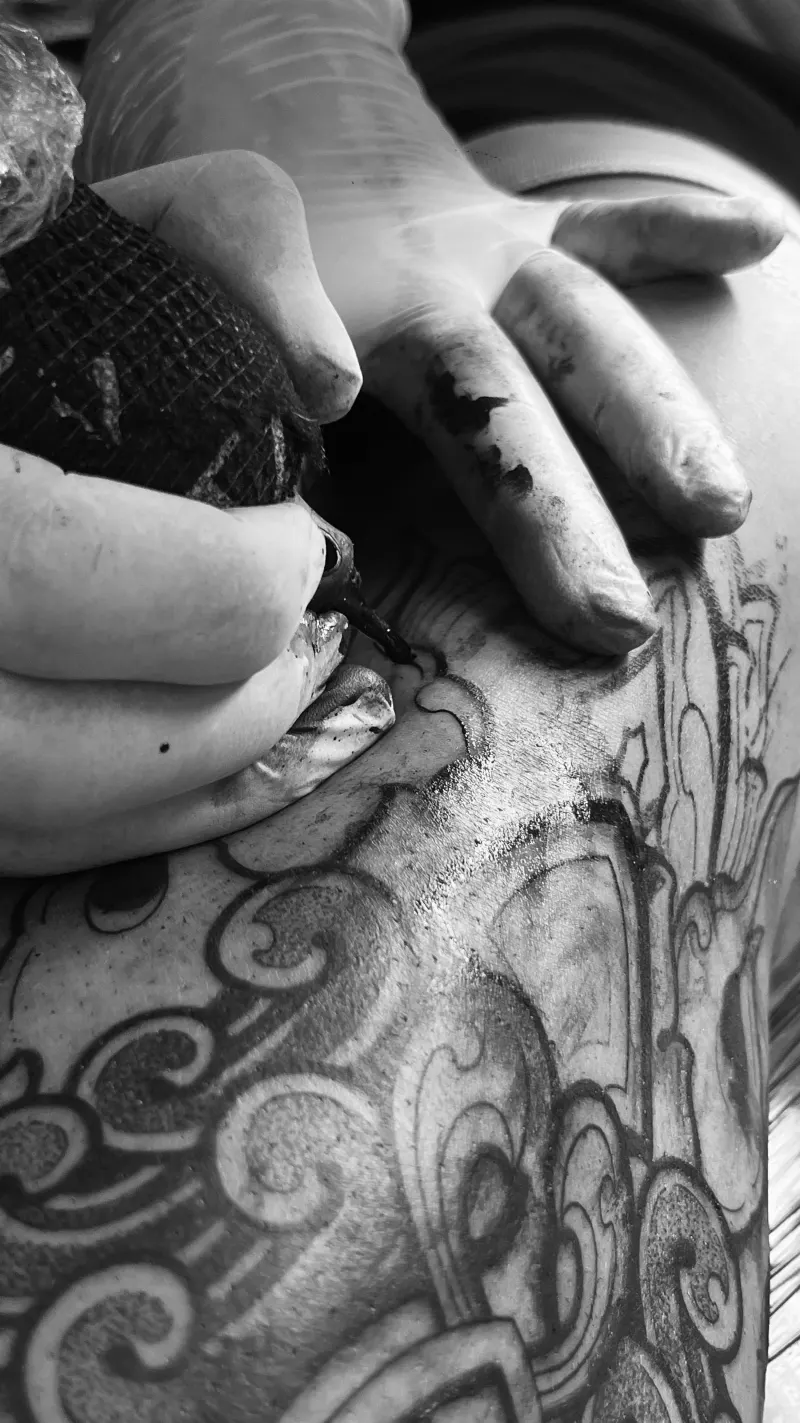 Motif ornemental en cours de tatouage, main tendant la peau, noir et blanc