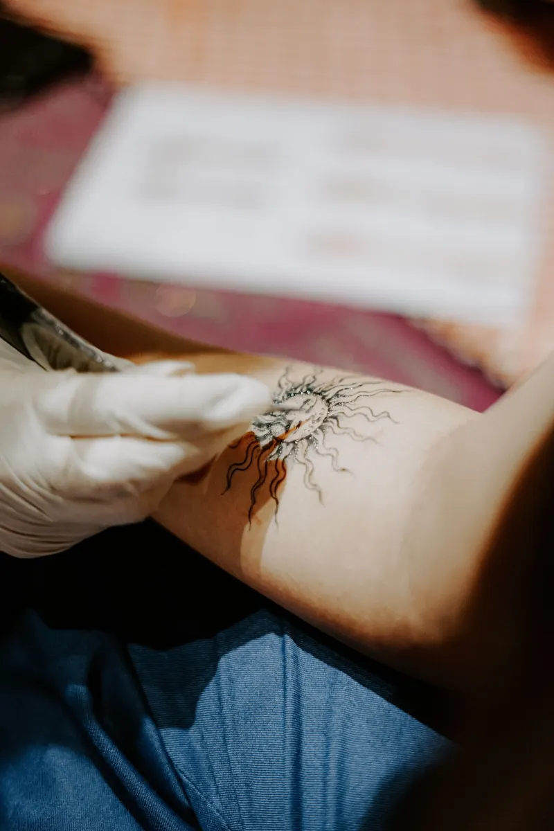 Petit soleil en trait fin juste tatoué, main gantée de blanc à côté