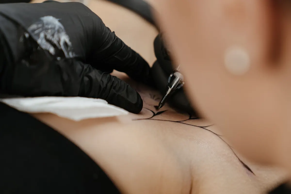 Main gantée de noir tenant la machine, premières lignes d’encre sur la peau