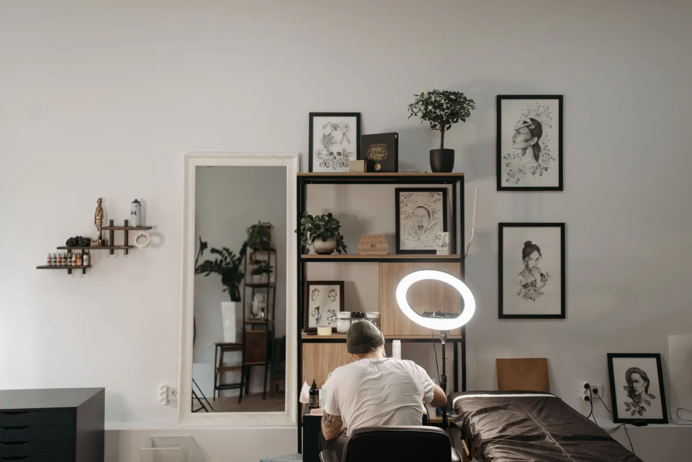 Coin du studio lumineux, étagères, plantes, dessins encadrés et lampe annulaire