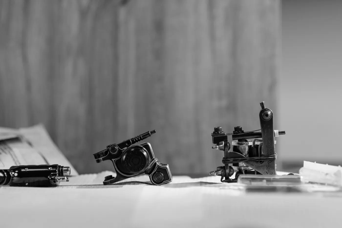Deux machines à tatouer posées sur une table blanche, noir et blanc