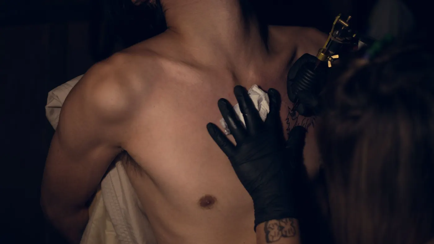 Main gantée de noir posée sur un torse pendant une séance, lumière tamisée