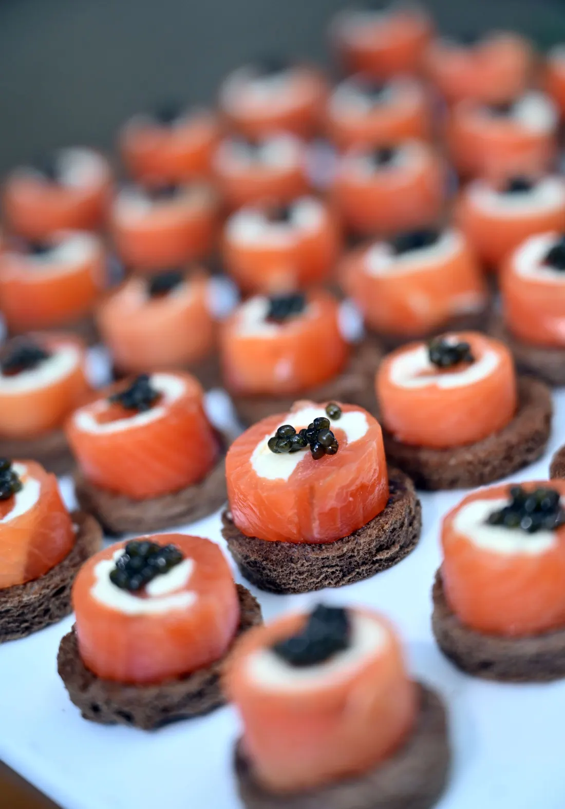 Bouchées de saumon fumé surmontées de caviar, alignées sur un plateau
