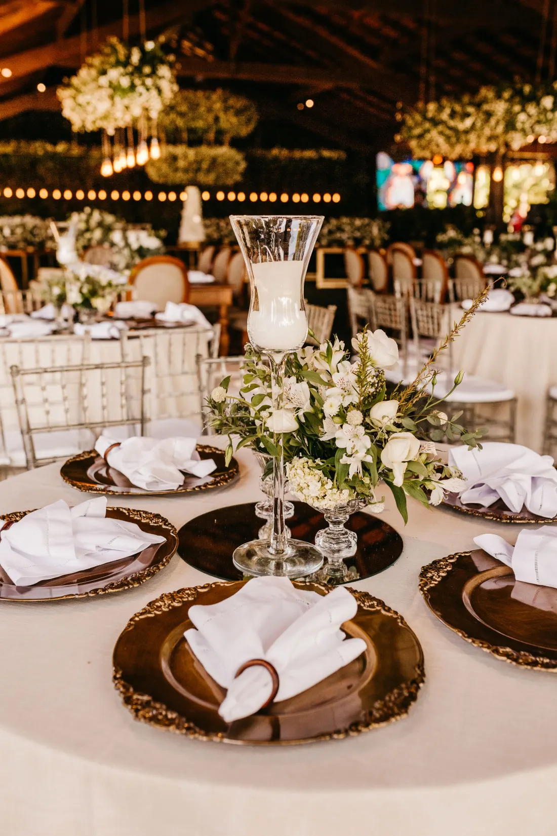 Table de mariage avec assiettes de présentation dorées, serviettes pliées et hautes compositions florales