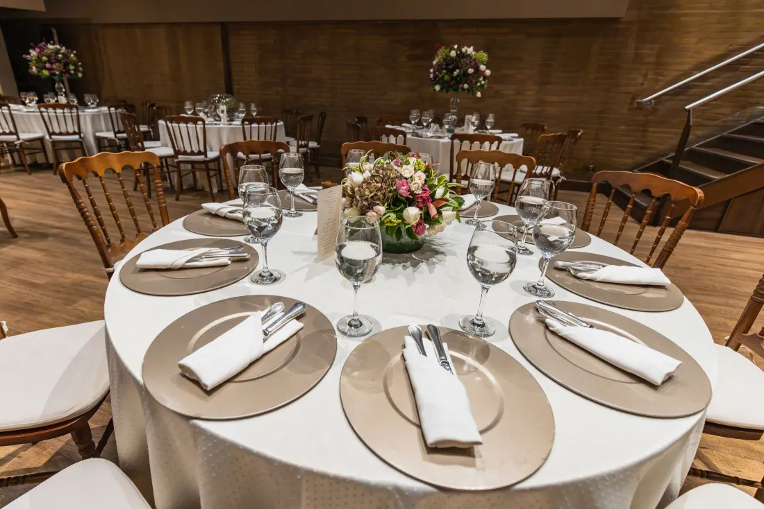 Table ronde dressée avec assiettes dorées, serviettes et verres à pied