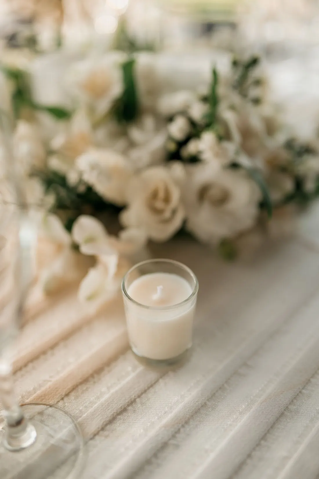 Composition de roses blanches et bougie sur un chemin de table clair